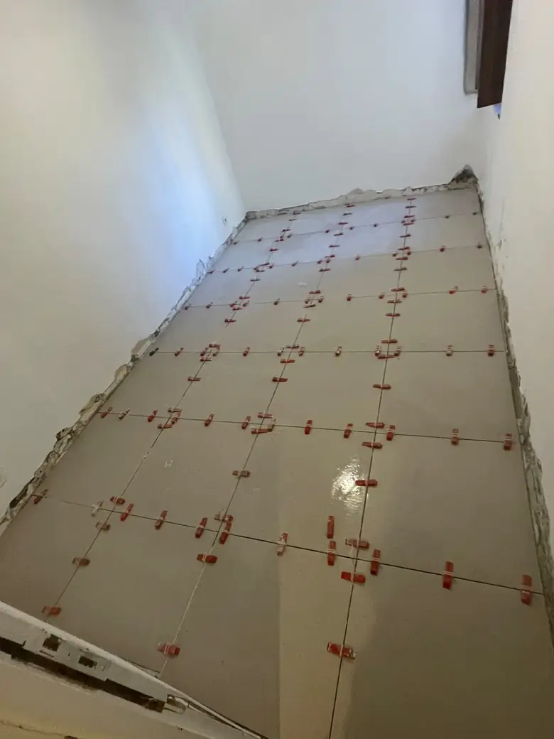 Pose de carrelage grand format en cours, croisillons de nivellement en place.