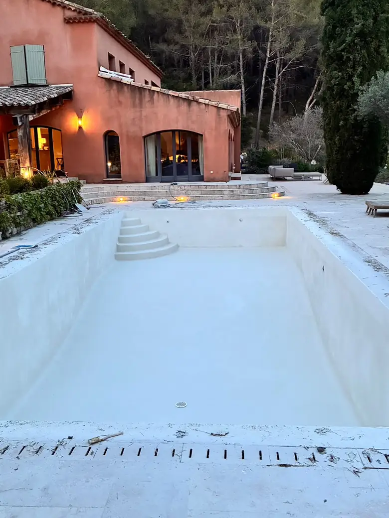 Rénovation d'une piscine devant une villa, bassin vidé et préparé.