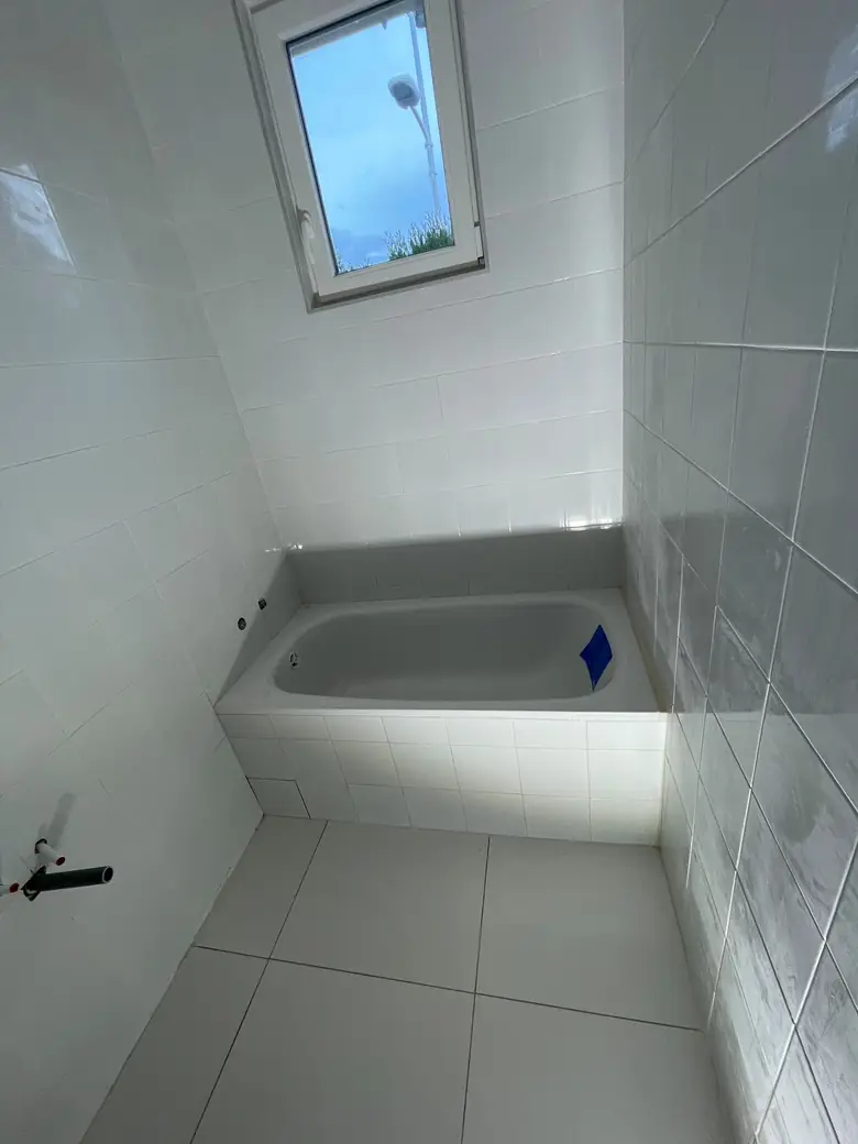 Salle de bain avec baignoire encastrée et faïence blanche grand format.