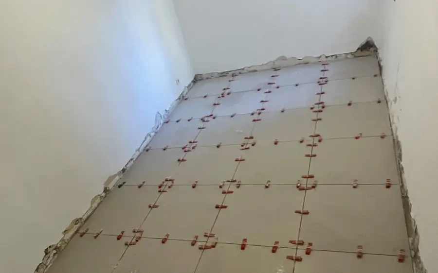 Pose de carrelage grand format en cours, croisillons de nivellement en place.