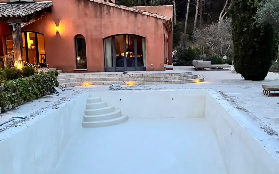 Rénovation d'une piscine devant une villa, bassin vidé et préparé.
